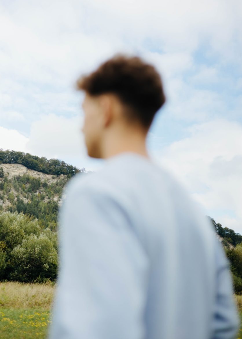 A man standing in a field looking at a hill