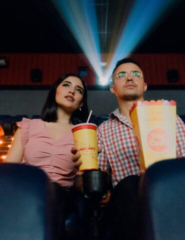 2 women sitting on blue leather chair holding white and red plastic cups